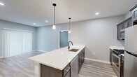 Located at 5510 Southwestern Blvd in Hamburg, NY, this well-appointed 2-bedroom, 2-bathroom residence offers a thoughtfully designed single-floor layout with modern finishes throughout. The open-concept kitchen and living area serves as the heart of the home, anchored by a generous white quartz island with an undermount sink and sleek matte black faucet. Dark espresso cabinetry, stainless steel appliances including a gas range and built-in microwave, and recessed lighting complete the kitchen, while pendant lights add a stylish touch above the island. Light-toned wood-look flooring flows through the main living areas, creating a bright and cohesive feel. The spacious primary bedroom features a sliding door with vertical blinds and direct access to a well-appointed en-suite bathroom, which includes a framed glass walk-in shower, a dark-cabinetry vanity with white countertop, and matching wood-look flooring. The second bedroom is carpeted and receives natural light through a large window with exterior views. A generously sized walk-in closet with built-in wire shelving provides ample storage. The secondary bathroom mirrors the refined aesthetic of the rest of the home. Recessed lighting and a neutral gray palette unify the space with a clean, contemporary ambiance.