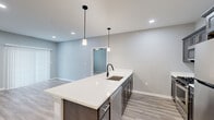 Located at 5510 Southwestern Blvd in Hamburg, NY, this well-appointed 2-bedroom, 2-bathroom residence offers a thoughtfully designed single-floor layout with modern finishes throughout. The open-concept kitchen and living area serves as the heart of the home, anchored by a generous white quartz island with an undermount sink and sleek matte black faucet. Dark espresso cabinetry, stainless steel appliances including a gas range and built-in microwave, and recessed lighting complete the kitchen, while pendant lights add a stylish touch above the island. Light-toned wood-look flooring flows through the main living areas, creating a bright and cohesive feel. The spacious primary bedroom features a sliding door with vertical blinds and direct access to a well-appointed en-suite bathroom, which includes a framed glass walk-in shower, a dark-cabinetry vanity with white countertop, and matching wood-look flooring. The second bedroom is carpeted and receives natural light through a large window with exterior views. A generously sized walk-in closet with built-in wire shelving provides ample storage. The secondary bathroom mirrors the refined aesthetic of the rest of the home. Recessed lighting and a neutral gray palette unify the space with a clean, contemporary ambiance.