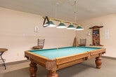 Located at 305 Margaret Ave in Kitchener, Ontario, this community amenity room is a generously sized, single-floor space designed to foster social interaction and recreational activity among residents. The room is thoughtfully arranged into distinct functional zones, making excellent use of its open layout.

At the heart of the space sits a full-size pool table with a classic oak finish, illuminated by a brass-and-green pendant light fixture suspended from the textured ceiling above. Cue racks and bar-height seating are neatly positioned nearby, completing the billiards area.

Adjacent to the billiards zone is a comfortable lounge area furnished with plush sofas arranged around a wooden coffee table. A wall-mounted television and an upright piano add to the entertainment options, creating an inviting atmosphere for relaxation and casual gatherings.

A dedicated library corner features tall, well-stocked bookshelves filled with a wide variety of titles, catering to a range of reading interests. Bright flush-mounted ceiling fixtures ensure the entire space is well-lit throughout.

Glass-paneled double doors connect the main room to an adjoining space that appears to function as a dining or meeting area, further extending the amenities available. Neutral-toned carpeting and light-colored walls contribute to a clean, welcoming ambiance throughout.