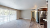 This single-floor residence offers a thoughtfully laid-out living space with a clean, neutral aesthetic throughout. The open living area is generously sized, featuring plush carpeting, warm beige walls, a textured ceiling, and large sliding glass doors fitted with vertical blinds that invite abundant natural light and provide views of surrounding greenery. The transition from carpet to wood-look vinyl flooring marks the entry and kitchen zones, creating a clear and functional separation of spaces.

The kitchen is a standout feature, showcasing rich dark-toned cabinetry, light speckled countertops, and stainless steel appliances including a range with microwave above. A peninsula-style counter opens toward the entry area, which is accented by a ceiling fan and recessed lighting, lending the space a comfortable, practical feel.

The bedroom is a calm, carpeted retreat with its own large window dressed in vertical blinds, offering natural light and outdoor views. The bathroom is neatly finished with wood-look flooring, a dark vanity with a light countertop, and a tub-shower combination. White trim and baseboards run consistently throughout the unit, tying together the cohesive and modern interior design. The overall ambiance is bright, clean, and move-in ready.