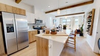 Located at 2500 Bobby Foster Rd SE in Albuquerque, NM, this thoughtfully designed one-bedroom, one-bathroom residence combines modern aesthetics with warm, natural materials. The open-concept kitchen and living area serves as the heart of the home, anchored by a large island with a white quartz countertop and natural wood cabinetry. Stainless steel appliances, including a side-by-side refrigerator with ice maker, an electric range, and a built-in microwave, complete the well-equipped kitchen. Exposed wood ceiling beams add architectural character, while light hardwood flooring flows seamlessly throughout the space. Pendant lighting over the island enhances the inviting atmosphere. The living area is bathed in natural light through tall vertical windows and a sliding glass door that opens to a private balcony with outdoor views. The bedroom offers a serene retreat with a large window, a sliding closet, and clean white walls. The full bathroom features a tub-shower combination and open shelving for convenient storage. An in-unit washer and dryer adds everyday practicality. The overall ambiance is bright, airy, and contemporary, reflecting a cohesive design sensibility suited for modern living in Albuquerque.