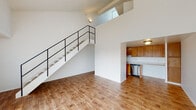 This two-story residence offers a thoughtfully designed layout across two levels, combining open living spaces with functional, well-appointed rooms throughout. The main level centers around a bright, open living area distinguished by soaring double-height ceilings and warm hardwood-style flooring that extends throughout the lower floor. A sleek staircase with black metal railings ascends to the upper level, serving as a striking architectural focal point. Large vertical-blind-covered sliding doors flood the living area with natural light. The galley-style kitchen features warm wood cabinetry, light stone countertops, stainless steel appliances including a dishwasher, refrigerator, and range, all complemented by hardwood-style flooring. Also on the main level is a full bathroom with a tiled shower-tub combination, wood-look flooring, and louvered closet doors adding a classic touch. A hallway half-bath provides additional convenience, featuring a vanity with a mirrored medicine cabinet. Upstairs, the carpeted bedrooms offer a quiet retreat, with vaulted ceilings and tall windows drawing in natural light. One bedroom includes a built-in wall niche, adding a unique design detail. The upper level maintains the airy, open feel established throughout the home, making this a well-balanced and functional two-story space.