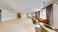 Located in Dover, NH, this thoughtfully designed single-floor common area offers a polished and contemporary environment spanning a generous footprint. The space is anchored by an open lobby lounge that sets a refined tone, featuring large windows dressed with layered drapes that flood the area with natural light and offer views of the surrounding landscape. Comfortable seating—including tufted leather sofas, velvet accent chairs, and a central coffee table atop a decorative area rug—creates an inviting gathering space. A sleek linear fireplace set into a textured stone accent wall adds warmth and visual interest.

Light-toned large-format tile flooring runs throughout, lending a clean, cohesive aesthetic to every area. The two hallways are bright and well-proportioned, with crisp white walls, recessed lighting, and gold-toned light fixtures that provide elegant accent illumination. A dedicated mailbox alcove features a wall of numbered unit mailboxes set against a dramatic dark surround with subtle under-lighting. An elevator vestibule, finished with warm taupe wall treatments and a stylish sputnik-style pendant fixture, provides convenient vertical access. The office is appointed with its own distinctive lighting and furnishings, completing a space that balances function with sophisticated design.