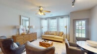 This single-floor residence offers a thoughtfully designed layout that balances comfort and functionality. The living room serves as the heart of the home, bathed in natural light streaming through a bank of large windows dressed with sheer white curtains and adjustable blinds. A ceiling fan with integrated lighting anchors the space, complemented by track lighting and wood-toned flooring that adds warmth throughout. The room comfortably accommodates a neutral sofa, accent chairs, a rustic wood coffee table, and a mid-century style dresser with a decorative mirror, creating an inviting and cohesive aesthetic.

The kitchen features rich, dark wood cabinetry, light countertops, and black appliances including a gas range, microwave, and dishwasher, all efficiently arranged for ease of use.

The primary bedroom is carpeted and well-lit, with a ceiling fan and wall-mounted sconce lighting flanking a upholstered headboard. Framed artwork adds a personal touch. The second bedroom mirrors this comfort with plush carpet, a ceiling fan, and multiple windows allowing generous natural light.

Both bathrooms are finished with light quartz-style countertops, undermount sinks, brushed nickel fixtures, and one features a full soaking tub with shower. The overall ambiance throughout is calm, neutral, and move-in ready.