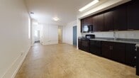 Located at 1003 28th St in Newport News, Virginia, this single-floor unit offers a functional and modern layout designed for comfortable everyday living. The open-concept living and kitchen area forms the heart of the space, featuring polished concrete-style flooring that runs throughout, lending an industrial yet clean aesthetic. The kitchen is well-appointed with rich dark wood cabinetry, granite countertops, a stainless steel undermount sink with a pull-down faucet, and black appliances including a refrigerator, range, and over-the-range microwave. Ample upper and lower cabinet storage ensures plenty of room for organization. The open living area adjacent to the kitchen provides generous space, enhanced by recessed and flush-mount lighting and a window that draws in natural light. A hallway connects the living areas to the private quarters and two full bathrooms. Each bathroom features a tub-shower combo with chrome fixtures, a dark-cabinetry vanity with a single sink and light countertop, and consistent flooring that ties into the rest of the unit. The overall design palette — neutral walls, dark cabinetry, and warm-toned flooring — creates a cohesive and contemporary atmosphere throughout.