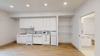 Located on the third floor at 2274 Newport Blvd in Costa Mesa, California, Unit 306 is a thoughtfully designed studio that maximizes functionality within a compact footprint. The open main living area features light wood-look flooring, clean white walls, and recessed lighting that keeps the space feeling bright and airy. A window with vertical blinds allows natural light to filter in while offering views of surrounding greenery, and a wall-mounted HVAC unit provides climate control.

The kitchen runs along one full wall and is outfitted with an abundance of tall white cabinetry extending to the ceiling, offering generous storage. A coil-top electric range, under-counter refrigerator, microwave, and a single-basin sink provide all essential appliances for everyday use. Countertop space flanks the range on both sides, enhancing practicality.

The bathroom is finished with a clean, all-white aesthetic and smooth flooring. It is fully ADA-accessible, featuring multiple stainless steel grab bars positioned near the toilet and along the walls, a white vanity with under-sink storage, and a bathtub/shower combination. The layout prioritizes ease of mobility and accessibility throughout. Overall, the unit presents a clean, functional, and well-maintained living space suited for a range of needs.