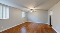 This single-floor unit offers a thoughtfully organized layout across five distinct spaces: a living room, bedroom, kitchen, bathroom, and hallway. Warm-toned hardwood flooring runs consistently throughout the main living areas and bedroom, lending a cohesive and inviting character to the space.

The living room is generously proportioned relative to the unit's overall footprint, featuring a ceiling fan with integrated lighting and multiple windows dressed with horizontal and vertical blinds, allowing natural light to filter in effectively. Neutral gray-toned walls complement the flooring throughout.

The bedroom offers comfortable dimensions, also finished with hardwood flooring, a window for natural light, and notable dual bi-fold closets providing ample storage. A hallway connects the key areas of the unit with convenient access to each room.

The kitchen features warm wood cabinetry with ample upper and lower storage, laminate countertops, a stainless steel sink, and white appliances including a stove and refrigerator, all set on hardwood-style flooring.

The bathroom includes tile flooring, a wood-toned vanity with storage, a white countertop, a large mirror, and a tub-shower combination, completing this functional and cohesive unit.