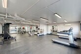Located at 730 Germantown Cir in East Ridge, Tennessee, this fitness center offers a well-organized and fully equipped exercise room designed to support a wide range of workout routines. The space is finished with a clean, utilitarian aesthetic — white walls, exposed overhead ductwork, and bright linear fluorescent lighting that ensures consistent illumination throughout.

The durable diamond-plate rubber flooring provides secure footing across the entire floor, while full-length mirrored walls along multiple sides visually expand the room and allow users to monitor their form during exercise. Large horizontal windows along one wall invite natural light and offer views of the surrounding outdoor landscape.

The cardio zone features multiple treadmills and elliptical machines, providing ample options for aerobic training. The strength and functional training area includes a cable resistance machine, an adjustable bench, TRX suspension straps, and a variety of free weights and accessories such as stability balls. A dedicated open area offers space for stretching, floor exercises, or mat-based workouts.

Additional amenities include a water fountain, wall-mounted equipment storage, and clearly marked exit access. A motivational wall graphic reading "Stronger Yesterday" adds an encouraging touch to the overall atmosphere. The fitness center is thoughtfully arranged to accommodate multiple users simultaneously, making it a practical and versatile facility.
