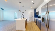 Located at 22100 E Quincy Ave in Aurora, CO, this single-floor, 2-bedroom, 2-bathroom residence offers a thoughtfully designed layout with modern finishes throughout. Light wood-tone flooring flows consistently across the open living spaces, complemented by crisp white walls and black hardware accents that add a contemporary edge.

The kitchen serves as a standout centerpiece, featuring bold navy blue lower cabinetry contrasted by white upper cabinets, a geometric hexagonal tile backsplash, stainless steel appliances, and a large center island with pendant lighting and an undermount sink with a matte black pull-down faucet. The kitchen opens seamlessly into the living area, creating an inviting, connected space.

The primary bedroom is generously sized, fitted with a ceiling fan and multiple windows offering views of the surrounding greenery. An elegant arched hallway leads to the primary bathroom, which includes a dual-sink navy vanity with white countertops, gold hardware accents, and a backlit LED mirror above tile-accented walls. A soaking tub and a walk-in closet complete the suite.

The second bedroom is bright and well-proportioned, benefiting from natural light through large windows. A private balcony provides outdoor access, while a dedicated laundry room and utility room add practical convenience. Four closets ensure ample storage throughout the residence.