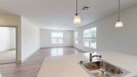 This single-floor unit offers a clean, modern design with a thoughtful open-concept layout. The heart of the home is the kitchen, which features warm honey-toned wood cabinetry, light quartz countertops, stainless steel appliances including a range, microwave, refrigerator, and dishwasher, and a central island with a built-in sink and pendant lighting overhead. The kitchen flows seamlessly into a generous living area bathed in natural light from multiple windows with views of the surrounding outdoors. Light wood-look flooring runs throughout the main living spaces, contributing to a bright and airy atmosphere. The bedrooms are carpeted in soft, neutral tones, providing a comfortable retreat, with windows that allow natural light to fill each room. Two bathrooms serve the unit — a full bathroom featuring a walk-in shower, single vanity with white cabinetry, and tile flooring, and a second bathroom with a similarly clean, white vanity and tile floor. A dedicated laundry area houses a full-sized washer and dryer, adding practical convenience to daily living. Throughout the unit, crisp white walls and consistent finishes create a cohesive, move-in-ready environment well-suited for comfortable everyday living.