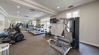 Located in Henrico, VA, this well-appointed fitness center offers a comprehensive exercise environment within a single, thoughtfully designed space. The room features a tray ceiling with recessed lighting and textured finishes, creating a polished and inviting atmosphere. Large windows along multiple walls flood the interior with natural light, while full-length mirrors visually expand the space and allow users to monitor their form during workouts.

The facility is equipped with a robust selection of cardio machines, including multiple treadmills and elliptical trainers, arranged in orderly rows to maximize usability and flow. A stationary bike and additional aerobic equipment round out the cardio offerings. Strength training is supported by a multi-station cable machine and a dedicated free weights area visible in the mirror reflections. Wall-mounted flat-screen televisions provide entertainment options during workouts.

The flooring consists of durable, neutral-toned carpet tiles well-suited for a high-traffic exercise environment. Glass-paned doors open to an outdoor area, further enhancing the sense of openness and connection to the exterior. The overall design balances functionality with a clean, modern aesthetic, making this fitness center a practical and welcoming resource.