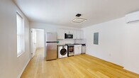 Located at 139 E Clifton Ave in Cincinnati's Clifton neighborhood, this one-bedroom, one-bathroom unit offers a efficiently designed single-floor layout with clean, modern finishes throughout. Light oak hardwood flooring runs continuously through the open living area and bedroom, lending warmth and visual continuity to the space.

The kitchen anchors the main living area and is outfitted with white shaker cabinetry, dark countertops, and a classic white subway tile backsplash. Stainless steel appliances include a refrigerator, range, over-the-range microwave, and dishwasher. An in-unit front-loading washer is also integrated into the kitchen area, adding a practical convenience. A modern square LED flush-mount fixture illuminates the space from above.

The bedroom is a well-proportioned room featuring two windows that invite natural light and a view of the surroundings. A wall-mounted mini-split HVAC unit provides individualized climate control. The room's white walls and hardwood floors maintain the clean, minimal aesthetic found throughout the unit.

The bathroom is thoughtfully finished with white subway tile surrounding a full soaking tub with a sliding glass enclosure, a wall-mounted medicine cabinet mirror, and a floating wood-toned vanity with an integrated sink. Tile flooring completes the polished look. A bold red entry door visible in the floorplan view adds a distinctive design touch to the unit's entrance.