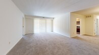 Located at 101 Kenilworth Park Dr in Towson, MD, this single-floor unit offers three bedrooms, two bathrooms, a living room, and a kitchen across a comfortable and functional floor plan. The living room is generously proportioned, featuring plush carpeting, neutral cream walls, and a large sliding glass door fitted with vertical blinds that allows abundant natural light to fill the space. The kitchen is outfitted with light wood cabinetry, granite-style countertops, stainless steel appliances including a refrigerator, range, and microwave, and easy-to-maintain hardwood-style flooring. An adjoining dining or flex area benefits from additional windows and connects seamlessly to the rest of the unit. The spacious primary bedroom features dual windows that bring in ample natural light and is finished with soft wall-to-wall carpeting. The two additional bedrooms are similarly appointed with carpet flooring and windows providing natural light. Both bathrooms are finished with stone-look tile flooring, warm wood vanities with white countertops, mirrored medicine cabinets, and brushed nickel fixtures. A dedicated closet provides additional storage. The unit presents a clean, well-maintained interior with a consistent neutral palette throughout.