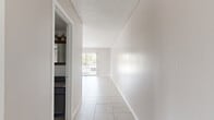 Located at 8100 Bellaire Blvd in Houston, TX, this one-bedroom, one-bathroom unit offers a well-organized single-floor layout with consistent light tile flooring and neutral warm-gray walls throughout. An entrance hallway leads into the open living and dining area, which benefits from natural light streaming through a sliding glass door fitted with vertical blinds, providing access to an outdoor area. The living room features a textured ceiling and a ceiling fan with integrated lighting, while the adjacent dining area is distinguished by decorative exposed ceiling beams and a chandelier pendant light fixture above, accompanied by a window overlooking the outdoors. The kitchen is efficiently appointed with gray cabinetry, granite-style countertops, a textured stone tile backsplash, a white range, and a window that brings in additional natural light. The spacious primary bedroom includes a ceiling fan, a generously sized window, and two closets, offering ample storage. The bathroom features a full tub-shower combination with white tile surround. Throughout the unit, clean white trim, textured ceilings, and a cohesive neutral palette create a bright and functional living environment suited for everyday comfort.