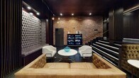 Located in the heart of Hollywood at 5529 Hollywood Blvd, this single-floor venue exudes a refined, moody elegance designed for an upscale entertainment experience. The space is divided into distinct areas, each with its own character while maintaining a cohesive, dramatic aesthetic throughout.

A central lounge area commands attention with an expansive wraparound tufted caramel sofa, accented by copper and globe pendant lights suspended from a dark ceiling. Polished dark floors and dark wood-paneled walls amplify the intimate ambiance, while tiered platform seating lines the perimeter.

An adjacent seating area features a striking exposed brick wall paired with a curated display cabinet, white barrel chairs, a marble-topped coffee table, and a tan tufted leather sofa — blending industrial warmth with contemporary refinement.

A more intimate private room is distinguished by dramatic floor-to-ceiling crimson velvet draping, a geometric honeycomb wood ceiling detail, and luxurious tufted velvet sofas in deep teal and silver. A large wooden table anchors the space, making it ideal for private gatherings.

Transitional corridors feature tufted wall panels and sleek vertical slat detailing, reinforcing the venue's cohesive, theatrical design language. Throughout, recessed lighting and carefully placed fixtures create a warm, atmospheric glow suited to Hollywood's iconic entertainment culture.
