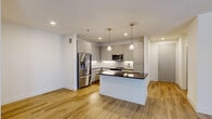 Located in Lewisville, TX, this well-appointed single-floor home offers three bedrooms and two bathrooms across a thoughtfully designed layout. The open-concept kitchen and living area serves as the heart of the home, anchored by a central island with a dark granite countertop, an undermount sink, and gold-toned hardware. Crisp white shaker cabinetry lines the walls, complemented by a white subway tile backsplash and a full suite of stainless steel appliances. Warm wood-look flooring flows throughout the main living areas, while pendant lighting with brass accents adds a modern, elevated touch. The bedrooms offer plush carpeting and vaulted ceilings with ceiling fans, creating a comfortable and airy atmosphere. Two closets provide practical storage solutions. The bathrooms are finished with granite-topped vanities, gold fixtures, and framed mirrors. One bathroom features a soaking tub with marble-look tile surround, while the other showcases a clean, modern design with ample vanity space. A connecting hallway ties the layout together efficiently. The overall palette of soft whites and warm neutrals gives the home a bright, clean, and contemporary feel.