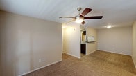 This single-story space in Tomball, Texas, offers a well-organized layout with a neutral color palette of warm beige tones throughout. The living area is generously sized, featuring plush carpeting, a ceiling fan with integrated lighting, and an open sightline to the kitchen, creating a connected and functional common area.

The kitchen is a standout feature, equipped with dark espresso cabinetry, dark granite-style countertops, a stone tile backsplash, and black appliances including a refrigerator, range, microwave, and dishwasher. Wood-look flooring runs through the kitchen, which opens to the living space via a breakfast bar with an overhead pass-through window. A door off the kitchen leads directly to an in-unit laundry area with shelving.

The bedrooms are carpeted and each includes a ceiling fan with light. One bedroom features windows and a glass-panel door offering natural light. The bathrooms are cleanly finished with white tiled tub-and-shower combinations, chrome fixtures, and wood-look flooring. The overall ambiance is practical and move-in ready, with consistent finishes carried throughout the space.