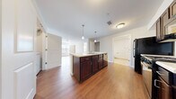 This single-floor residence offers a thoughtfully designed layout across three bedrooms and three full bathrooms, making it a practical and comfortable living space. The open-concept kitchen and living area serves as the heart of the home, highlighted by a central island with dark espresso cabinetry, a built-in sink, and pendant lighting overhead. The kitchen is further equipped with black appliances, including a refrigerator and range, along with ample counter and cabinet storage. Warm hardwood-style flooring flows throughout the main living areas, creating a cohesive and inviting ambiance.

The living room extends naturally from the kitchen, featuring a ceiling fan and windows fitted with blinds that allow for natural light. The bedrooms offer a mix of flooring options — some with plush carpeting and others with hardwood-style floors — and each is served by windows that bring in additional natural light. The primary bedroom provides a comfortable, well-sized retreat.

The three bathrooms are consistently finished with light tile flooring, dark wood vanities, white countertops, and tub-shower combinations. A dedicated in-unit laundry room with a full-size washer and dryer adds everyday convenience. Additional features include a hallway, closet, and a clean, neutral color palette throughout.