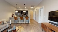 Located at 4111 E Ninth Ave in Denver, Colorado, this single-floor unit offers a well-designed, modern living space in the Park Hill neighborhood. The open-concept layout connects the kitchen and living area seamlessly, creating a cohesive and functional environment.

The kitchen is outfitted with dark, flat-front cabinetry, a light quartz countertop peninsula with bar seating for three, stainless steel appliances including a refrigerator, microwave, and range, and a dark tile backsplash. Pendant lighting in matte black anchors the space with a contemporary touch. Light wood-style flooring runs throughout the kitchen and living areas, reinforcing the modern aesthetic.

The living room is bright and airy, featuring oversized black-framed windows and a sliding glass door that opens to a private balcony with urban views. The room offers ample space for comfortable seating arrangements.

The bedroom is carpeted for warmth and comfort, with a large window providing natural light and city views, a sliding closet, and space for a dedicated work area.

The bathroom includes a full soaking tub with shower, framed by large-format gray wall tiles and light wood-style flooring, maintaining the clean, modern design consistent throughout the unit.
