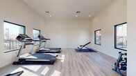 This well-appointed fitness center is designed with a clean, modern aesthetic that promotes an energizing workout environment. The space features light-toned hardwood-style flooring throughout, crisp white walls, and recessed ceiling lighting that contributes to a bright and open atmosphere.

The cardio zone is equipped with multiple NordicTrack treadmills positioned in front of a row of black-framed windows, allowing users to enjoy outdoor views while exercising. An elliptical machine and a stationary bike round out the cardio offerings, providing diverse options for aerobic training.

A dedicated strength and flexibility area includes an adjustable weight bench, a dumbbell rack, and a rowing machine, all positioned on protective rubber floor mats. The open layout ensures ample space between equipment, promoting safe and comfortable use.

Natural light pours in from multiple windows on two walls, including views overlooking an outdoor pool area and the surrounding community. The elevated ceilings lend a sense of spaciousness rarely found in fitness facilities of this type. A keyed entry door provides secure access, and safety equipment including a fire extinguisher is visibly mounted. The overall design is minimalist and functional, creating a focused environment well-suited for daily exercise routines.