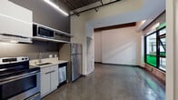 Located at 430 S Broadway in the heart of Downtown Los Angeles, this single-floor unit blends industrial character with modern finishes throughout. Polished concrete floors extend across the open living area, reflecting light and lending a sleek, urban aesthetic. Exposed wooden ceiling beams and open ductwork overhead nod to the building's historic industrial roots, while clean white walls provide a bright, contemporary contrast.

The kitchen is efficiently designed and fully equipped, featuring stainless steel appliances including a full-size refrigerator, electric range, dishwasher, and microwave. White flat-front cabinetry with matte black hardware and light countertops complete the contemporary kitchen aesthetic, with overhead strip lighting ensuring a well-lit workspace.

The main living area is anchored by a wall of large, black-framed industrial windows that flood the space with natural light and offer views into the building's surrounding corridor. The open layout provides flexibility for a variety of uses.

The bathroom is finished with floor-to-ceiling white subway tile surrounding a full soaking tub and shower combination, complemented by brushed nickel fixtures and a frosted window for natural light. The polished concrete flooring continues seamlessly into this space. Overall, the unit delivers a distinctive loft-style atmosphere rooted in Downtown LA's vibrant urban core.