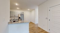 This well-designed 1-bedroom, 1-bathroom unit offers a thoughtfully laid-out single-floor plan that maximizes every square foot. The open-concept kitchen and living area serves as the heart of the home, featuring light gray shaker-style cabinetry, a white subway tile backsplash, and granite countertops that extend to a peninsula with an integrated sink — ideal for casual dining or meal prep. A full suite of stainless steel appliances, including a side-by-side refrigerator with water and ice dispenser, an electric range, and an over-the-range microwave, completes the kitchen. Warm, medium-toned hardwood-style flooring flows seamlessly throughout the entire unit, creating a cohesive and inviting aesthetic. The living area is bright and open, with a glass door and adjacent window that invite natural light and provide outdoor access. A hallway connects the main living spaces to the private bedroom, which is equipped with a ceiling fan and a closet. The full bathroom features a granite-topped vanity with an undermount sink and a tub-shower combination. Clean white walls and recessed lighting throughout contribute to a fresh, modern ambiance.