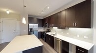 This single-floor residence showcases a contemporary design with a cohesive aesthetic carried throughout each space. The kitchen serves as a central highlight, featuring rich dark espresso cabinetry that extends to the ceiling for generous storage, paired with crisp white quartz countertops for a striking contrast. A large central island provides additional prep space and casual seating. Stainless steel appliances, including a French door refrigerator with an in-door ice and water dispenser, a gas range, built-in microwave, and dishwasher, equip the kitchen for everyday functionality. A subtle glass tile backsplash adds texture, while pendant lighting above the island and track lighting overhead create a well-lit workspace.

The open living area flows naturally from the kitchen, finished with wood-look flooring, crown molding, and neutral-toned walls that create a bright and welcoming atmosphere. A large window invites natural light into the living space. The bedrooms are generously sized, each benefiting from large windows with exterior views. The bathroom features a wide dark-cabinet vanity, an expansive mirror with overhead lighting, and a clean, neutral palette that contributes to a calm, functional environment.