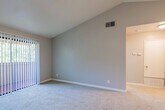 This single-story residence is defined by its striking vaulted ceilings, which lend an open, airy quality to the main living area. The living room is generously proportioned, finished with plush carpet, and anchored by a fireplace with glass doors. A sliding glass door fitted with vertical blinds provides natural light and outdoor access, while a pendant light and ceiling fan contribute to the room's functionality and ambiance.

The kitchen is a practical highlight, featuring white cabinetry, stone-look countertops, and a full suite of stainless steel appliances including a gas range, microwave, and refrigerator. A skylight brightens the kitchen naturally, and wood-look flooring runs throughout the cooking and dining areas. A breakfast bar connects the kitchen to the living space, creating an open flow. In-unit laundry with a full-size top-loading washer and dryer is conveniently housed in a dedicated closet off the main hall.

The bedroom is well-sized, carpeted, and benefits from corner windows that allow ample natural light. The bathroom is cleanly appointed with a granite-look vanity, large wall mirror, wood-look flooring, and accessibility grab bars. A connecting hallway with additional storage ties the layout together cohesively.