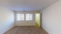 This single-floor residential unit presents a clean, functional layout designed for comfortable everyday living. The living area is spacious and open, finished with neutral-toned wall-to-wall carpeting that extends throughout the main rooms, creating a warm and cohesive feel. Large windows with blinds allow natural light to flow into the space, enhancing the bright, airy atmosphere. A front entry door opens directly into the living area, which also features convenient access to additional rooms via interior doorways.

The galley-style kitchen is efficiently organized with white cabinetry lining both sides, offering ample storage above and below the counter. It is equipped with a white electric range, a refrigerator, a built-in dishwasher, and a double-basin sink, all set on light tile flooring. A ventilation hood above the range adds to the kitchen's practical design.

The bedroom is generously sized and features a wide sliding-door closet with a full-width hanging rod, providing substantial storage. Carpeted flooring continues throughout, maintaining a consistent, comfortable aesthetic.

The bathroom includes a vanity with light wood cabinetry, a white countertop, and a mirror above, complemented by tile flooring. A utility panel is also visible within the space, adding to the unit's self-contained nature. Overall, the layout is practical, well-lit, and move-in ready.
