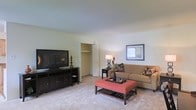 Located at 26 N Ladow Ave in Millville, New Jersey, this single-story space offers a straightforward and functional layout designed for comfortable everyday living. The living area serves as the central gathering space, showcasing wall-to-wall carpeting in a neutral tone that adds warmth underfoot. The room is generously proportioned, providing ample space for a full seating arrangement alongside a large entertainment setup. Light-colored walls throughout create a clean, bright backdrop that complements the overall interior. A built-in closet with double doors offers convenient storage directly within the living area, adding to the unit's practicality. The ceiling is smooth and standard in height, contributing to the room's understated, easy-to-furnish character. Natural light filters into the space, keeping the atmosphere open and inviting. The overall ambiance is calm and residential, with a neutral palette that lends itself well to a variety of décor styles. The single-floor design ensures easy accessibility throughout, making it a practical and comfortable option for those seeking a low-maintenance living space in Millville, NJ.