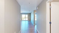 Located at 4901 Broadway in Oakland, CA, this well-appointed 2-bedroom, 2-bathroom residence offers a thoughtfully designed single-level layout. A wide entryway hallway with warm hardwood-style flooring leads into the open living area, which is bathed in natural light from large windows overlooking the surrounding neighborhood. The combined kitchen and living room forms the heart of the home, featuring a sleek, modern kitchen outfitted with rich dark wood cabinetry, stainless steel appliances including a full-size refrigerator, microwave, and range, as well as a kitchen island with a crisp white countertop — ideal for both cooking and casual dining. The living area flows seamlessly from this space, maintaining a bright and airy ambiance. Both bedrooms offer plush carpeting, generous closet space with built-in hanging rods, and large windows that bring in ample daylight and street-level views of Oakland. The two bathrooms are finished in clean, neutral tones; one features a full tub and shower combination with white subway tile surround and light tile flooring. Additional storage is provided by two dedicated closets. The overall palette of soft grays, warm wood tones, and white trim creates a clean, contemporary aesthetic throughout.