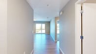 Located at 4901 Broadway in Oakland, CA, this well-appointed 2-bedroom, 2-bathroom residence offers a thoughtfully designed single-level layout. A wide entryway hallway with warm hardwood-style flooring leads into the open living area, which is bathed in natural light from large windows overlooking the surrounding neighborhood. The combined kitchen and living room forms the heart of the home, featuring a sleek, modern kitchen outfitted with rich dark wood cabinetry, stainless steel appliances including a full-size refrigerator, microwave, and range, as well as a kitchen island with a crisp white countertop — ideal for both cooking and casual dining. The living area flows seamlessly from this space, maintaining a bright and airy ambiance. Both bedrooms offer plush carpeting, generous closet space with built-in hanging rods, and large windows that bring in ample daylight and street-level views of Oakland. The two bathrooms are finished in clean, neutral tones; one features a full tub and shower combination with white subway tile surround and light tile flooring. Additional storage is provided by two dedicated closets. The overall palette of soft grays, warm wood tones, and white trim creates a clean, contemporary aesthetic throughout.