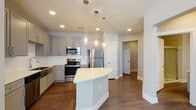 Located at 1426–1448 E Mockingbird Lane in Midland, Texas, this thoughtfully designed single-story residence blends contemporary finishes with functional living. The heart of the home is a well-appointed kitchen featuring grey shaker-style cabinetry, a crisp white subway tile backsplash, a stainless steel farmhouse sink, and a full suite of stainless steel appliances including a refrigerator, range, microwave, and dishwasher. A curved quartz-topped island anchors the space and is illuminated by a trio of elegant glass pendant lights, complementing the recessed lighting throughout. Rich wood-look flooring flows through the main living and kitchen areas, adding warmth and cohesion. The bedrooms are finished with plush carpet, neutral grey walls, and ceiling fans, with windows that invite natural light. Closet space is provided via sliding-door closets with built-in hanging rods. The bathrooms are finished with grey vanities, white quartz countertops, and large-format tile surrounds — one offering a tub-shower combination and another featuring a glass-enclosed walk-in shower. A dedicated laundry area with shelving provides added convenience. The overall aesthetic is clean, modern, and move-in ready.
