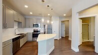 Located at 1426–1448 E Mockingbird Lane in Midland, Texas, this thoughtfully designed single-story residence blends contemporary finishes with functional living. The heart of the home is a well-appointed kitchen featuring grey shaker-style cabinetry, a crisp white subway tile backsplash, a stainless steel farmhouse sink, and a full suite of stainless steel appliances including a refrigerator, range, microwave, and dishwasher. A curved quartz-topped island anchors the space and is illuminated by a trio of elegant glass pendant lights, complementing the recessed lighting throughout. Rich wood-look flooring flows through the main living and kitchen areas, adding warmth and cohesion. The bedrooms are finished with plush carpet, neutral grey walls, and ceiling fans, with windows that invite natural light. Closet space is provided via sliding-door closets with built-in hanging rods. The bathrooms are finished with grey vanities, white quartz countertops, and large-format tile surrounds — one offering a tub-shower combination and another featuring a glass-enclosed walk-in shower. A dedicated laundry area with shelving provides added convenience. The overall aesthetic is clean, modern, and move-in ready.