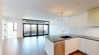 Located at 1930 35th St in Denver, CO, this contemporary residence offers six bedrooms and two bathrooms across a single floor. The open-concept kitchen and living area serves as the heart of the home, showcasing dark stone countertops, white flat-panel cabinetry, a glass backsplash, and a statement brass range hood. A kitchen island with a brass faucet and undermount sink anchors the space, complemented by a modern pendant light fixture. Floor-to-ceiling sliding glass doors connect the living area to a private balcony, filling the space with natural light and framing expansive views of the Denver skyline and surrounding greenery. Hardwood flooring runs throughout the main living areas, while bedrooms feature plush carpeting. Several bedrooms offer large black-framed windows with impressive city and waterway views. The primary bedroom includes direct balcony access via sliding glass doors. Two well-appointed bathrooms feature marble-style tile, floating wood vanities, brass fixtures, and glass-enclosed walk-in showers. Storage is thoughtfully provided through two closets, including a spacious walk-in closet with built-in shelving and drawers, as well as an additional closet with in-unit washer access. The overall aesthetic is clean, modern, and sophisticated.