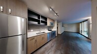 Located in Seattle's vibrant Capitol Hill neighborhood, Unit 316 at 721 E Pine Street offers a thoughtfully designed, single-floor residence with a contemporary aesthetic throughout. The open-concept kitchen and living area serves as the heart of the unit, featuring rich dark hardwood-style flooring and a well-appointed kitchen equipped with stainless steel appliances — including a full-size refrigerator, electric range, dishwasher, and over-the-range microwave. Warm wood-toned cabinetry is complemented by sleek white quartz countertops and open upper shelving, lending a modern, urban feel. Track lighting illuminates the kitchen and entry area efficiently. The living space benefits from large floor-to-ceiling windows and a sliding glass door that flood the room with natural light and open onto views of a lush, landscaped courtyard, creating a calm and inviting atmosphere. The bathroom is finished with the same modern sensibility, featuring a wide floating vanity with ample storage, clean tile flooring, and a glass-enclosed shower. Wall sconces provide warm, accent lighting. Throughout the unit, neutral tones, clean lines, and quality finishes create a cohesive and functional living environment well-suited to urban life in Seattle.