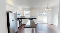 This spacious 3-floor home offers a thoughtfully designed layout that balances functionality and modern style. The kitchen serves as a standout feature, showcasing crisp white shaker cabinetry that extends to the ceiling, striking dark granite countertops, and a full suite of stainless steel appliances including a refrigerator, range, microwave, and dishwasher. A central island provides additional prep space and casual seating, making it an ideal hub for cooking and entertaining. Rich, dark hardwood flooring runs throughout, creating a warm contrast against the bright white cabinetry and light-filled interior. Recessed lighting illuminates the kitchen, complemented by natural light streaming through multiple windows and a sliding glass door that opens directly onto a covered outdoor deck — offering seamless indoor-outdoor living. The vaulted ceiling adds an airy, open feel to the main level. With three floors of living space, this home provides ample room for a variety of needs, from everyday living to hosting guests. The overall ambiance is clean, contemporary, and inviting, with a neutral palette that provides a versatile backdrop for any interior style.