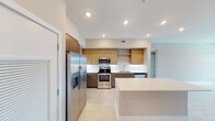 This contemporary single-floor residence offers a thoughtfully designed layout with clean lines and a cohesive neutral palette throughout. The kitchen serves as a standout feature, showcasing a combination of warm wood-toned upper cabinetry and sleek taupe lower cabinets, complemented by a crisp white backsplash and light countertops. A full suite of stainless steel appliances — including a side-by-side refrigerator with ice dispenser, electric range, built-in microwave, and dishwasher — provides a fully equipped cooking environment. Open shelving adds a modern touch, while a kitchen island offers additional prep and dining space. Light tile flooring flows consistently throughout the common areas, enhancing the sense of openness and continuity. The bedrooms are bright and airy, each featuring ceiling fans, neutral warm-toned walls, and large windows that invite natural light and outdoor views. The primary bathroom is generously proportioned, offering a dual-sink vanity with a wide mirror, a glass-enclosed walk-in shower with tile surround, and a separate soaking tub framed by large-format tiles. A second bathroom mirrors the clean, modern aesthetic with equally refined finishes. The overall ambiance is calm, contemporary, and move-in ready.