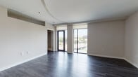 The Peach is a well-appointed 1-bedroom, 1-bathroom residence located in Atlanta's 30309 corridor, offering a thoughtfully designed single-floor layout with a clean, modern aesthetic throughout. The living area is spacious and open, highlighted by rich dark hardwood flooring, neutral warm-toned walls, and a distinctive curved tray ceiling detail that adds architectural interest. Floor-to-ceiling windows and a glass-panel balcony door flood the space with natural light and provide sweeping outdoor views of the Atlanta skyline and surrounding greenery, with the private balcony offering a seamless indoor-outdoor connection. The open-concept kitchen is outfitted with high-gloss white cabinetry, dark countertops, a white subway tile backsplash, and a full suite of stainless steel appliances including a range, microwave, and dishwasher. The bedroom is generously sized with warm hardwood flooring, ample closet access, and proximity to the full bathroom. The bathroom features a soaking tub with marble-style tile surround, a wide vanity with dark countertop, an undermount sink, and large-format tile flooring. Together, these elements create a polished, contemporary living environment suited for comfortable urban living in Atlanta.