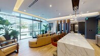 Located at 419 SE Second St in Fort Lauderdale, FL, this upscale single-floor space exemplifies contemporary design with a refined, hospitality-inspired aesthetic. The main lounge area is anchored by a striking white marble-veined counter, complemented by warm light wood flooring that runs throughout. Tall floor-to-ceiling glass walls flood the space with abundant natural light while offering views of lush palm trees and the outdoor surroundings, creating a seamless indoor-outdoor connection.

Richly toned vertical wood panel dividers elegantly partition the open layout into distinct seating zones, each thoughtfully furnished with designer pieces — including curved sofas, velvet accent chairs in deep blue, and sculptural occasional tables. Recessed cove lighting and globe pendant chandeliers add a warm, layered glow to the tray ceilings above.

A quieter lounge alcove features charcoal walls contrasted by light furnishings, sculptural art pieces, and framed geometric wall art, lending an intimate gallery-like quality. Elsewhere, a curated wall display of bold black-and-white abstract canvases anchors a casual seating nook with low-profile chairs and metallic accent stools. A serene windowed nook with sheer draping provides a private retreat. Lush tropical plants are thoughtfully placed throughout, reinforcing the vibrant South Florida ambiance.