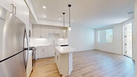 Located at 1445 Town Center Dr in Chula Vista, CA, this well-appointed 2-bedroom, 1-bathroom residence offers a thoughtfully designed layout with modern finishes throughout. The open-concept kitchen is a standout feature, showcasing light gray cabinetry, white quartz countertops, a subway tile backsplash, a central island with pendant lighting, and a full suite of stainless steel appliances including a gas range, microwave, dishwasher, and refrigerator. The kitchen flows seamlessly into the living area, which is bathed in natural light from large windows and features warm-toned luxury vinyl plank flooring. The primary bedroom includes plush carpeting, a ceiling fan, and sliding glass door access to a private balcony with outdoor views. A walk-in closet with built-in shelving adds practical storage. The second bedroom also features carpet flooring and light-filled windows. Both rooms are served by a full bathroom with a tiled tub-shower combo, a single-sink vanity, and built-in wall shelving. An in-unit stacked washer and dryer is conveniently accessible from the hallway. Clean white walls, recessed lighting, and consistent modern detailing create a bright, cohesive ambiance throughout the home.