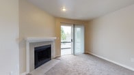 This single-floor residence offers a comfortable and practical layout with a warm, neutral color palette throughout. The living area is a welcoming space anchored by a tile-surround fireplace with a white mantel, providing a cozy focal point. A sliding glass door fitted with vertical blinds opens to a private balcony, allowing natural light to fill the room and offering views of surrounding greenery. Soft wall-to-wall carpeting runs throughout the living area, contributing to a relaxed ambiance.

The kitchen is designed for functionality, featuring white cabinetry with ample storage, light-toned countertops, and wood-look flooring. White appliances, including a range, refrigerator, and dishwasher, are neatly arranged within the galley-style layout. A peninsula with a sink connects the kitchen to the main living space, creating an open, flowing feel between the two areas.

The bathroom is clean and well-appointed, with a full tub and shower combo finished in white tile, complemented by wood-look flooring and a mirrored vanity. The space throughout maintains a bright, move-in-ready aesthetic with consistent neutral tones, making it a functional and inviting home.