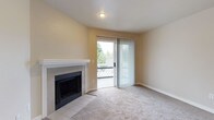 This single-floor residence offers a comfortable and practical layout with a warm, neutral color palette throughout. The living area is a welcoming space anchored by a tile-surround fireplace with a white mantel, providing a cozy focal point. A sliding glass door fitted with vertical blinds opens to a private balcony, allowing natural light to fill the room and offering views of surrounding greenery. Soft wall-to-wall carpeting runs throughout the living area, contributing to a relaxed ambiance.

The kitchen is designed for functionality, featuring white cabinetry with ample storage, light-toned countertops, and wood-look flooring. White appliances, including a range, refrigerator, and dishwasher, are neatly arranged within the galley-style layout. A peninsula with a sink connects the kitchen to the main living space, creating an open, flowing feel between the two areas.

The bathroom is clean and well-appointed, with a full tub and shower combo finished in white tile, complemented by wood-look flooring and a mirrored vanity. The space throughout maintains a bright, move-in-ready aesthetic with consistent neutral tones, making it a functional and inviting home.