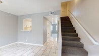 Located at 919 S Lyon St in Santa Ana, CA, this two-story, 2-bedroom, 2-bathroom home is thoughtfully laid out across two floors. The ground floor hosts the main living areas, including a combined living and dining room with warm tile flooring, textured walls painted in a cool gray tone, and a sliding glass door with vertical blinds that opens to a private patio, allowing natural light to flow in. The kitchen features white cabinetry, rich brown laminate countertops, a gas range, and matching tile flooring that ties the space together seamlessly. A staircase with blue-gray carpet and a clean white handrail leads to the upper level. Upstairs, the hallway connects two carpeted bedrooms, including a generously sized primary bedroom, each offering a calm, neutral palette. Both bathrooms are finished with white vanities, tile surround tub-shower combinations, and light flooring, presenting a clean and functional aesthetic. The upper floor also includes a balcony, two closets, and additional storage. Textured ceilings are consistent throughout the home, adding a classic character to each room.