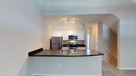 This two-floor home offers a thoughtfully designed layout that balances functionality and comfort. The kitchen serves as a central highlight, featuring a full suite of stainless steel appliances including a refrigerator, electric range, and over-the-range microwave. Crisp white cabinetry provides generous storage, while dark countertops offer a striking contrast that adds visual depth to the space. A curved breakfast bar peninsula extends the counter space and creates a natural division between the kitchen and the adjacent living area, making it ideal for casual dining or entertaining. Track lighting overhead ensures the kitchen is well-illuminated. The open-concept design allows for a seamless flow between the main living areas on the first floor. Neutral-toned walls and light carpeting contribute to a clean, bright ambiance throughout. A staircase connects the two levels, with the upper floor offering additional living space. The overall design emphasizes practicality with modern finishes, making this a move-in-ready home suited for a variety of lifestyles.