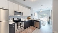 This efficiently designed one-bedroom, one-bathroom unit offers a thoughtfully organized single-floor layout that maximizes every square foot. Light wood-tone flooring flows consistently throughout the space, creating visual continuity and a clean, modern aesthetic.

The kitchen is a standout feature, showcasing a two-tone design with crisp white upper cabinetry and dark lower cabinets paired with light countertops. A full suite of stainless steel appliances — including a refrigerator, electric range, over-the-range microwave, and dishwasher — lines the L-shaped layout, which transitions seamlessly into the living area.

The living room benefits from a large sliding glass door that invites abundant natural light and provides outdoor access, creating an open and airy feel. A ceiling fan adds both function and style overhead.

The bedroom features a broad window with outdoor views, allowing generous natural light to fill the compact but functional space. The bathroom offers a full-width vanity with white cabinetry, a large mirror, and a shower/tub combination. A dedicated walk-in closet accessible from the bathroom provides valuable storage. The entryway includes an additional closet, completing the practical layout.