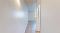 Located at 835 W Rosecrans Ave in Los Angeles, CA, this efficiently designed single-floor unit offers a well-organized layout that makes smart use of its compact footprint. The combined living, dining, and kitchen area forms the heart of the space, featuring light wood laminate flooring that runs throughout and crisp white walls that create a clean, bright atmosphere. A large window with vertical blinds in the living area welcomes natural light and provides a view of the surrounding greenery, enhancing the open feel of the room. The kitchen is neatly integrated into the main living space, equipped with white cabinetry, a range, and a sink — all finished in a consistent, understated palette. A textured ceiling adds subtle visual interest throughout the main area. A hallway connects the living space to the remaining rooms, including a full bathroom outfitted with a tiled shower/tub combination, grab bars, a toilet, and a single-sink vanity with white cabinetry. Additional storage is provided through a dedicated closet and a pantry, offering practical organizational options. The unit's straightforward, functional design and cohesive neutral finishes make it a practical and easy-to-maintain living space in the Gardena/South Los Angeles area.