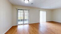 This two-story residence offers a practical and comfortable layout designed for everyday living. The main level features warm hardwood-style flooring that runs throughout the open living area, which is bathed in natural light through large sliding glass doors fitted with vertical blinds. A staircase leads to the upper floor, creating a clear separation between living and sleeping spaces. The galley-style kitchen is well-appointed with rich wood cabinetry lining both walls, generous counter space, a double-basin stainless steel sink, and white appliances including a gas range and refrigerator. The kitchen connects seamlessly to the living area, enhancing the overall flow of the main floor. Upstairs, the bedrooms feature plush wall-to-wall carpeting and neutral cream-toned walls, with windows providing outdoor views and allowing natural light to fill each room. The bathroom is finished with tile flooring, a granite-topped vanity with white cabinetry, and a full tub and shower combination enclosed by sliding glass doors. Throughout the home, textured ceilings, clean white trim, and a consistent neutral color palette create a cohesive and inviting atmosphere that is both functional and easy to personalize.