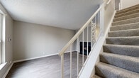 Located at 308 Plus Park Blvd in Nashville, TN, this two-story, 2-bedroom, 2-bathroom home offers a well-organized layout divided evenly across two floors. The main level features an open-concept living, dining, and kitchen area. The living room is highlighted by a dark-tiled fireplace and light wood-look flooring that extends throughout the main level, creating a clean, cohesive aesthetic. A sliding glass door with vertical blinds in the dining area allows natural light to fill the space. The kitchen is well-appointed with white shaker-style cabinetry, subway tile backsplash, white countertops, and a full suite of stainless steel appliances including a range, dishwasher, and refrigerator. Upstairs, both bedrooms feature plush carpeting and dedicated closets with built-in shelving for ample storage. The primary bedroom is generously sized, while the secondary bedroom includes a bright window with blinds. Each bathroom is finished with white vanities, white countertops, and framed mirrors with warm-toned accents. A carpeted staircase with a white railing connects the two floors. Textured ceilings and neutral warm-gray walls are consistent throughout, lending the home a fresh, move-in-ready feel.