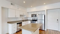 This single-floor residence features 2 bedrooms, 3 bathrooms, and 2 closets, thoughtfully arranged to maximize functionality and comfort. The open-concept kitchen and living area serves as the heart of the home, anchored by a central island with a neutral stone-toned countertop. The kitchen is outfitted with white shaker-style cabinetry, stainless steel appliances including a refrigerator, range, microwave, and dishwasher, complemented by matching countertops and wood-look flooring that flows throughout the common areas. The living room receives generous natural light through large windows that frame striking mountain views, creating a bright and airy atmosphere. Both bedrooms are carpeted and well-proportioned, each featuring windows that bring in natural light and views of the surrounding landscape. The primary bedroom includes access to a spacious walk-in closet with built-in hanging rods and shelving. The bathrooms feature white cabinetry with taupe countertops, large vanity mirrors, and tub-shower combinations with built-in shelving. Clean white walls and consistent neutral tones throughout give the space a modern, cohesive aesthetic.